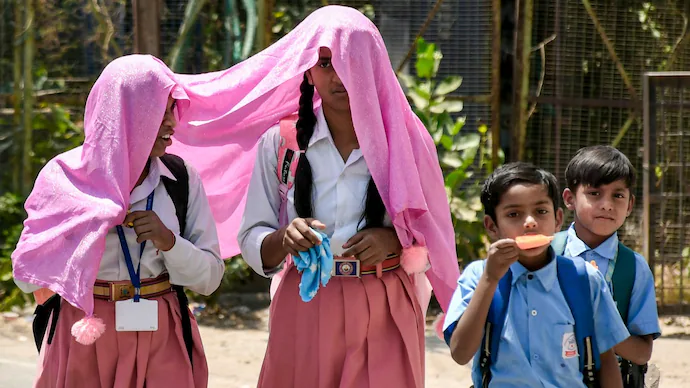 Students shield themselves from the scorching heat while returning from school. Several states have announced early summer holidays.